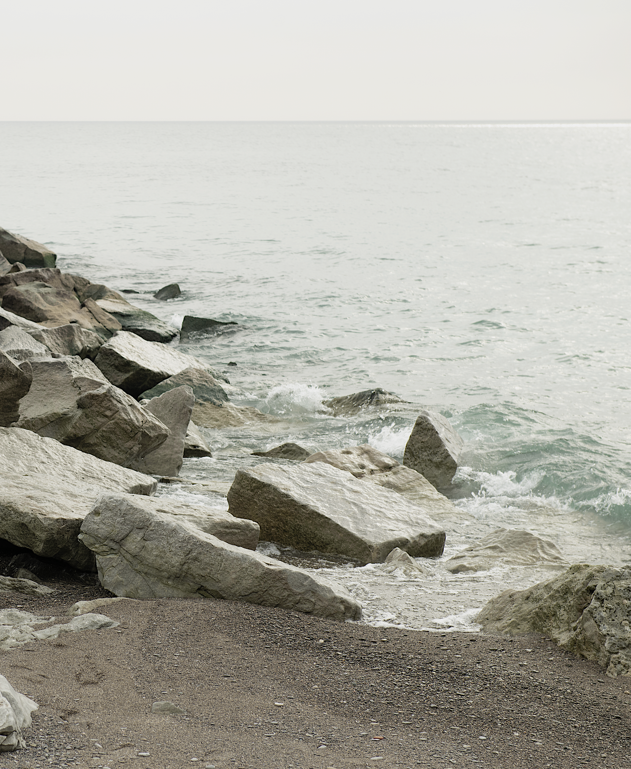 ALLWOOD photograph of pale water meeting rocks along the shore.